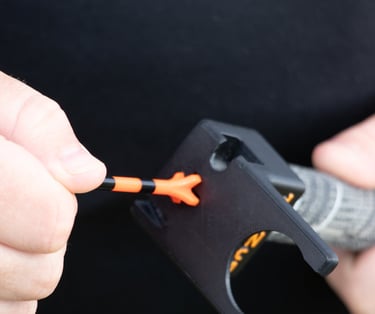 A close-up of a golfer's hand placing an orange golf tee into a 'TeeZup' tool attached to a club grip.