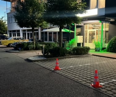 Illuminated entrance of Hotel Thannhof in Germany with a paved parking lot and classic cars.