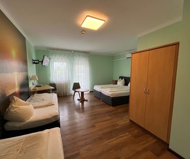 Spacious hotel room with twin beds, wooden wardrobe, desk area, and a large sunset wall mural.