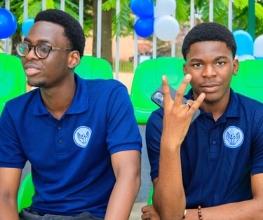 two men sitting on green chairs in front of a fence