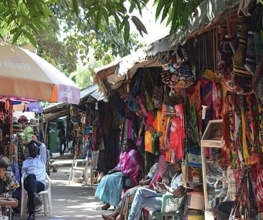 Lokale marktplaats in Gambia met kleurrijke kleding en handwerk onder parasols en afdakjes.
