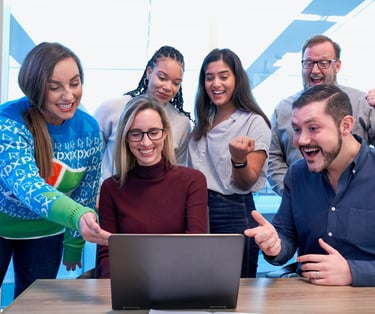 Diverse business team celebrating success while looking at a laptop in a modern office.