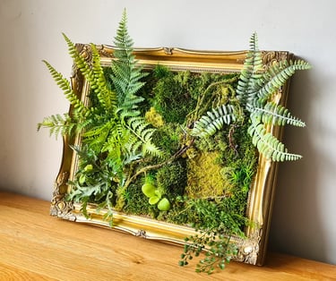 Framed preserved moss wall art with ferns in an ornate gold vintage frame on a wooden table.