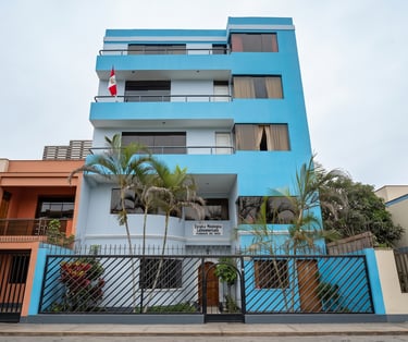 Exterior view of the blue Escuela Misiologica Latinoamericana building in Peru with palm trees and a gate.