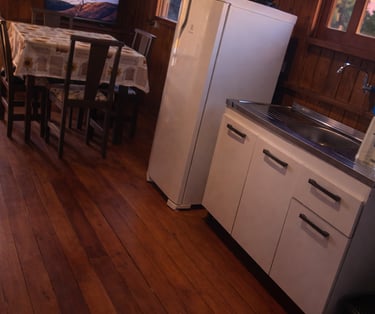 parte interna da cabana, a cozinha, com geladeira, pia, armários, mesa e TV 