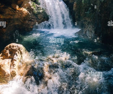a waterfall in the middle of a river with sun shining through the trees