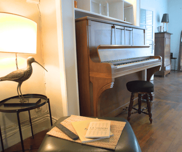 Espace de vie chaleureux avec piano en bois dans maison meublée pour groupes.