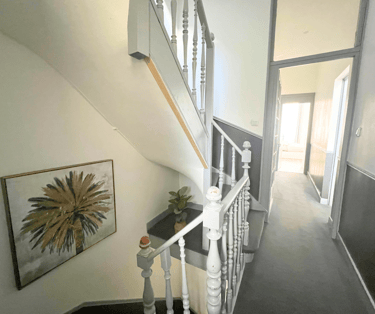 Couloir lumineux avec escalier en bois dans maison meublée spacieuse.