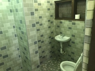 Small green tiled bathroom featuring a wall-mounted pedestal sink, toilet, and grey mosaic floor tiles.