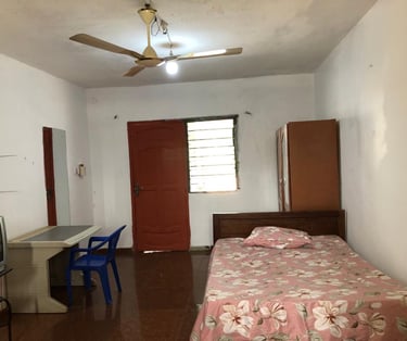 Basic guest room featuring a single bed with floral sheets, ceiling fan, and wooden furniture.