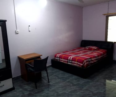 A simple bedroom featuring a bed with red plaid bedding, a wooden desk with a black chair, and a wardrobe.