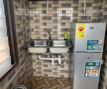 Double bowl stainless steel kitchen sink and silver Nasco refrigerator in a tiled room.