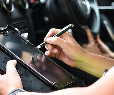 A driving examiner uses a stylus on a digital tablet to record results during a car driving test.