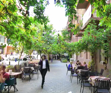 a woman walking down a sidewalk with people sitting at tables