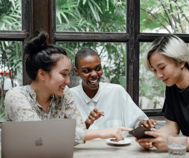 three people sitting at a table with a laptop having a conversation
