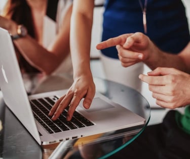 Persone che collaborano a un tavolo di vetro, indicando e digitando su un portatile.