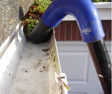 A curved gutter vacuum attachment cleaning debris and moss from a white residential gutter system.