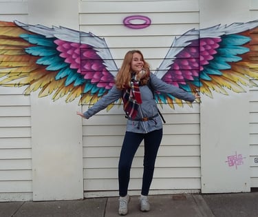 a woman standing in front of a wall with a large colorful angel wings