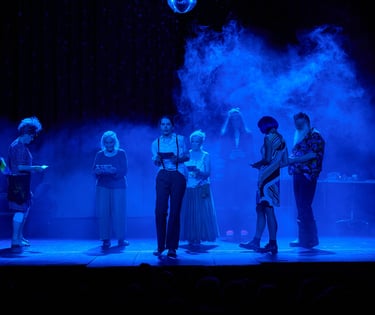 Eine blau beleuchtete Bühne mit Nebel. Verkleidete junge und ältere Menschen gehen umher.
