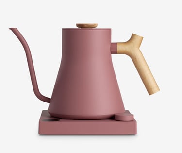 A matte pink electric gooseneck kettle with a wooden handle on a matching heating base.