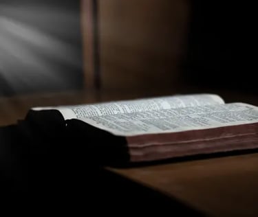  Bíblia aberta sobre mesa com feixe de luz iluminando suas páginas.