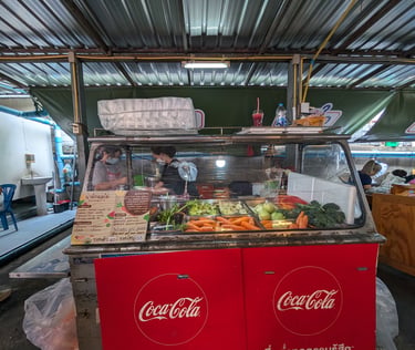 Street food vendor in Thailand preparing fresh fruit smoothies and juices at a Coca-Cola branded market stall.