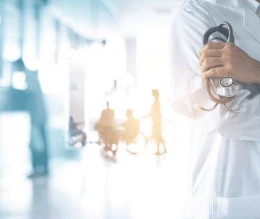A doctor in a white lab coat holds a stethoscope in a busy hospital hallway.