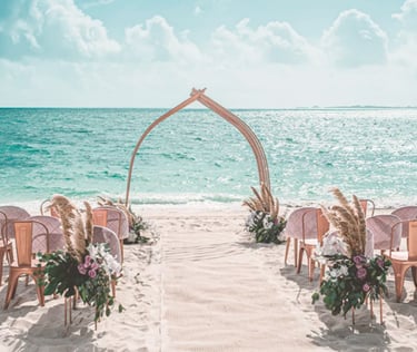 Elegant beach wedding ceremony setup with rose gold chairs and pampas grass decor overlooking the turquoise ocean.