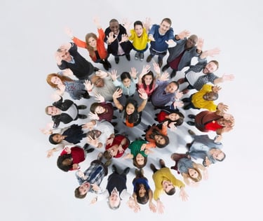 A diverse group of smiling people standing in a circle looking up and waving at the camera.