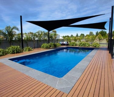 Modern rectangular pool with timber decking, deep blue water and grey stone coping tiles.