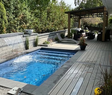 Modern lap pool with deep blue water and dark grey stone tiles, featuring a sleek waterfall wall