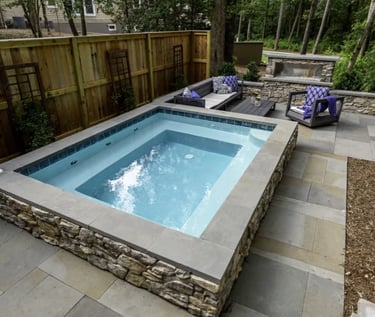 Raised square spa pool with pale blue water and grey stone coping and tiles in a modern garden setti