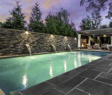 Modern rectangular lap pool with soft green water, dark stone wall and charcoal grey tiled surrounds