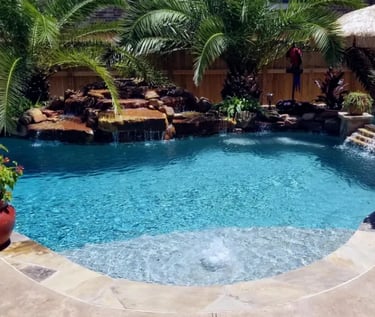 Curved tropical pool with rock waterfall, deep blue water and natural stone coping with pebble inter