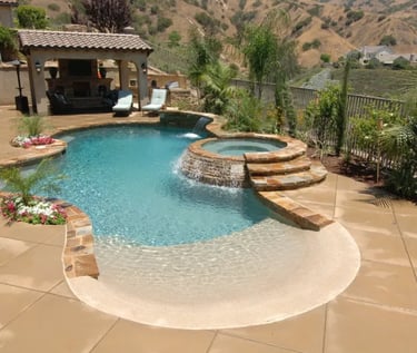 Freeform pool with raised spa, pale aqua water and natural sand-toned stone coping and interior.