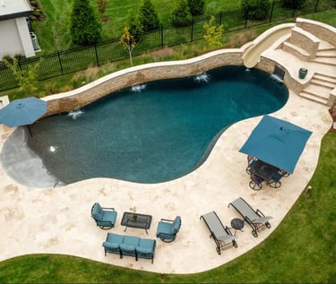 Freeform curved pool with deep teal water and dark mosaic tiles, edged with natural stone terraces