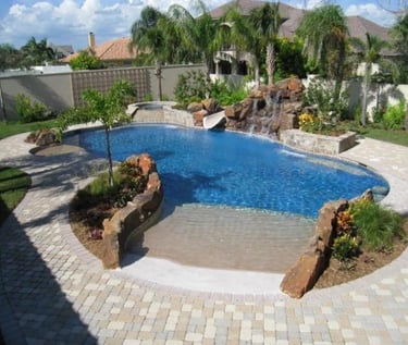 Natural lagoon pool with blue water, rock features and sandy-toned paving with subtle mosaic tiling