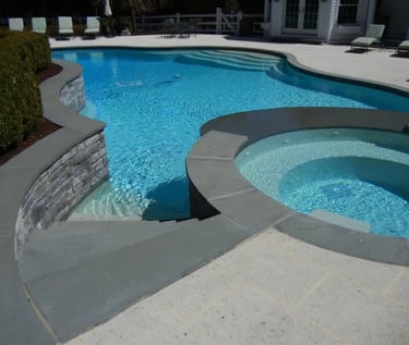 Curved pool and spa combo with light blue water, grey coping and matching grey interior tiles