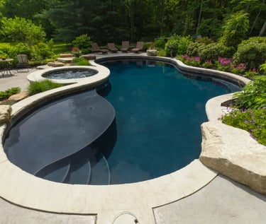 Freeform lagoon pool with dark blue water, smooth curves and light stone coping with dark interior t