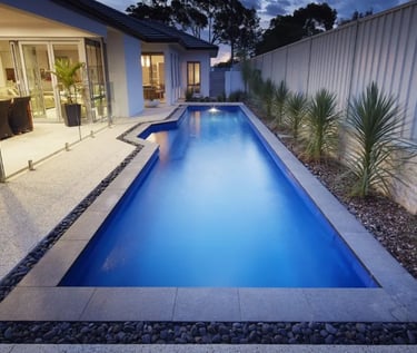 Rectangular backyard lap pool, deep blue water with dark blue mosaic tiles and stone coping.