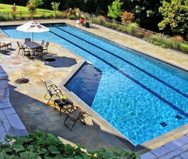 Long rectangular lap pool, clear blue water, pale stone coping with dark lane tile accents