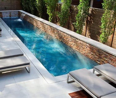 Narrow lap pool with deep blue water, stacked stone feature wall and neutral tile lining.