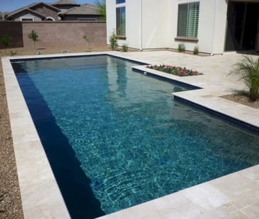 Geometric pool with deep blue water and light stone tiles set against a modern backyard.