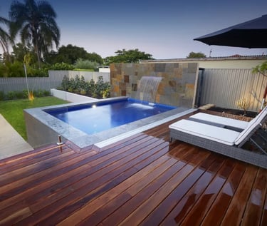 Raised plunge pool with waterfall, deep blue water and grey stone tiles