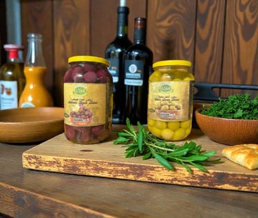 Glass jars of gourmet black and green olives on a rustic wooden cutting board with fresh herbs.