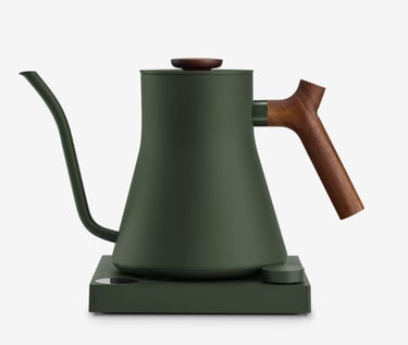 Matte green electric gooseneck kettle with walnut wood handle on a heating base.