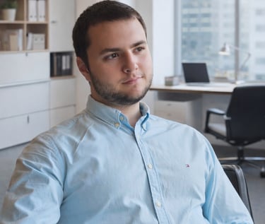 Professional businessman in a light blue button-down shirt sitting in a modern office.