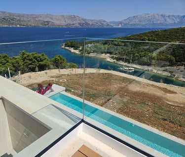Staklena ograda balkona sa pogledom na uvalu i more