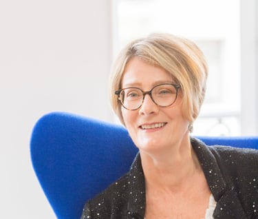a woman in glasses and a black jacket sitting in a chair