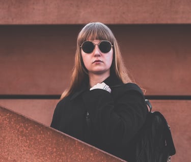 a woman in sunglasses and a black jacket standing in between a wall and a staircase